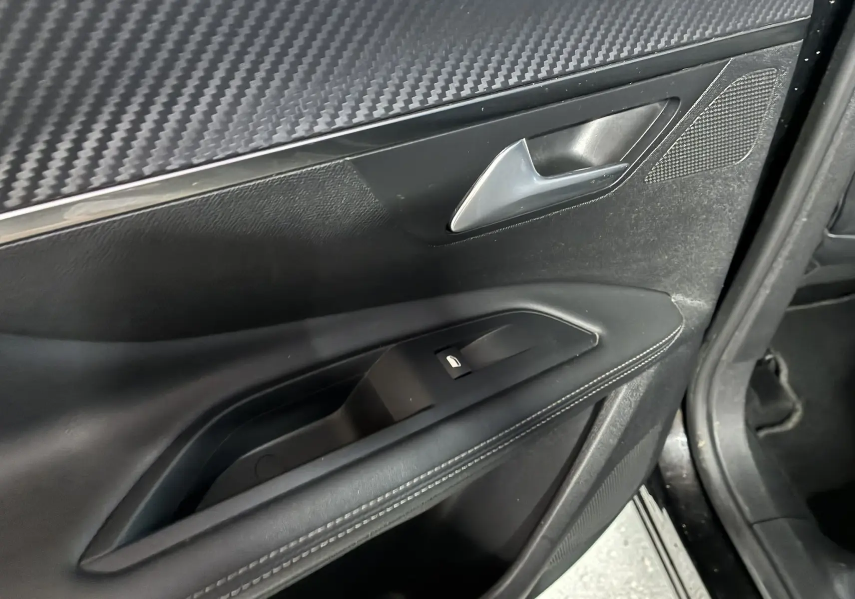 Gros plan sur la porte intérieure côté gauche d’un Peugeot 3008 noir, avec poignée argentée et bouton de vitre électrique.