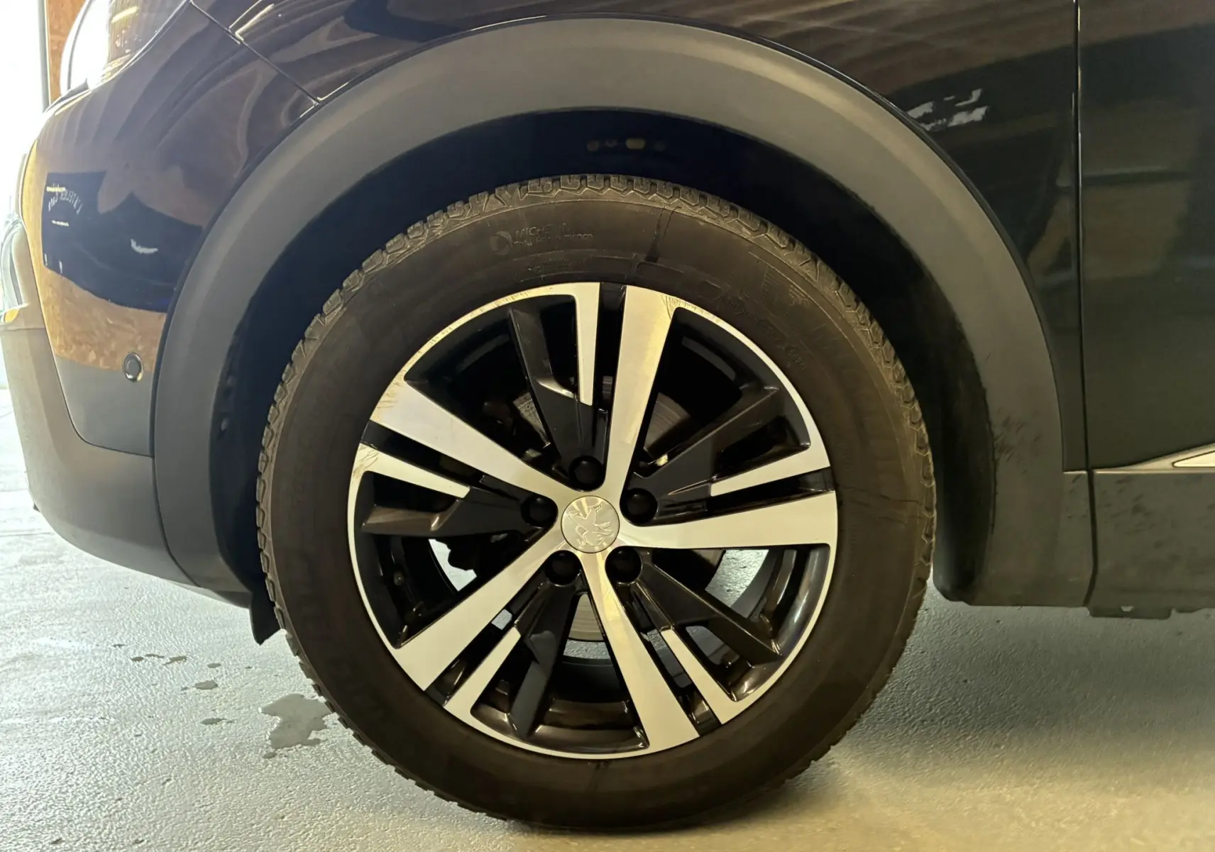 Gros plan sur la roue avant gauche du Peugeot 3008 noir de 2020 avec jante alliage bicolore moderne.