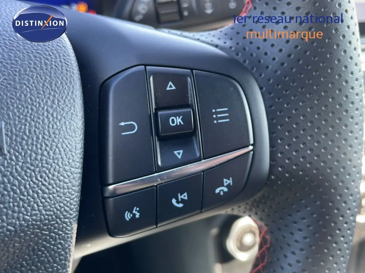 Gros plan sur les commandes multifonctions noires du volant perforé côté gauche d’un Ford Puma gris Solar Metal.