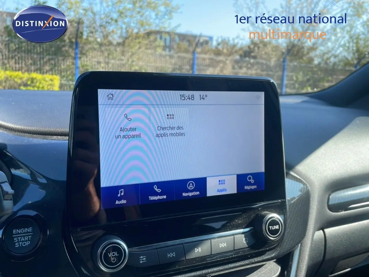 Vue intérieure centrée sur l’écran tactile du tableau de bord d’une Ford Puma gris Solar Metal, avec commandes audio visibles.