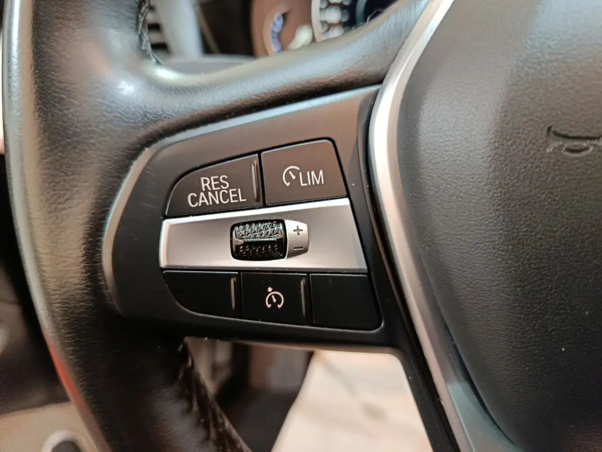 Gros plan sur les commandes de régulateur de vitesse et limiteur sur le volant cuir noir du BMW X3 xDrive30e gris foncé.