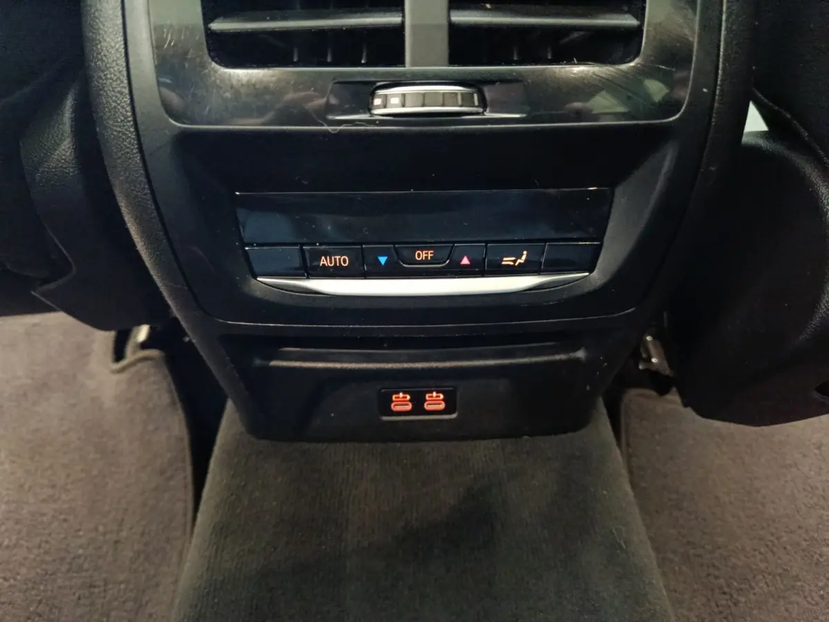 Détail de la console arrière noire du BMW X3 xDrive30e 2020 avec commandes climatisation et prises USB éclairées rouges.