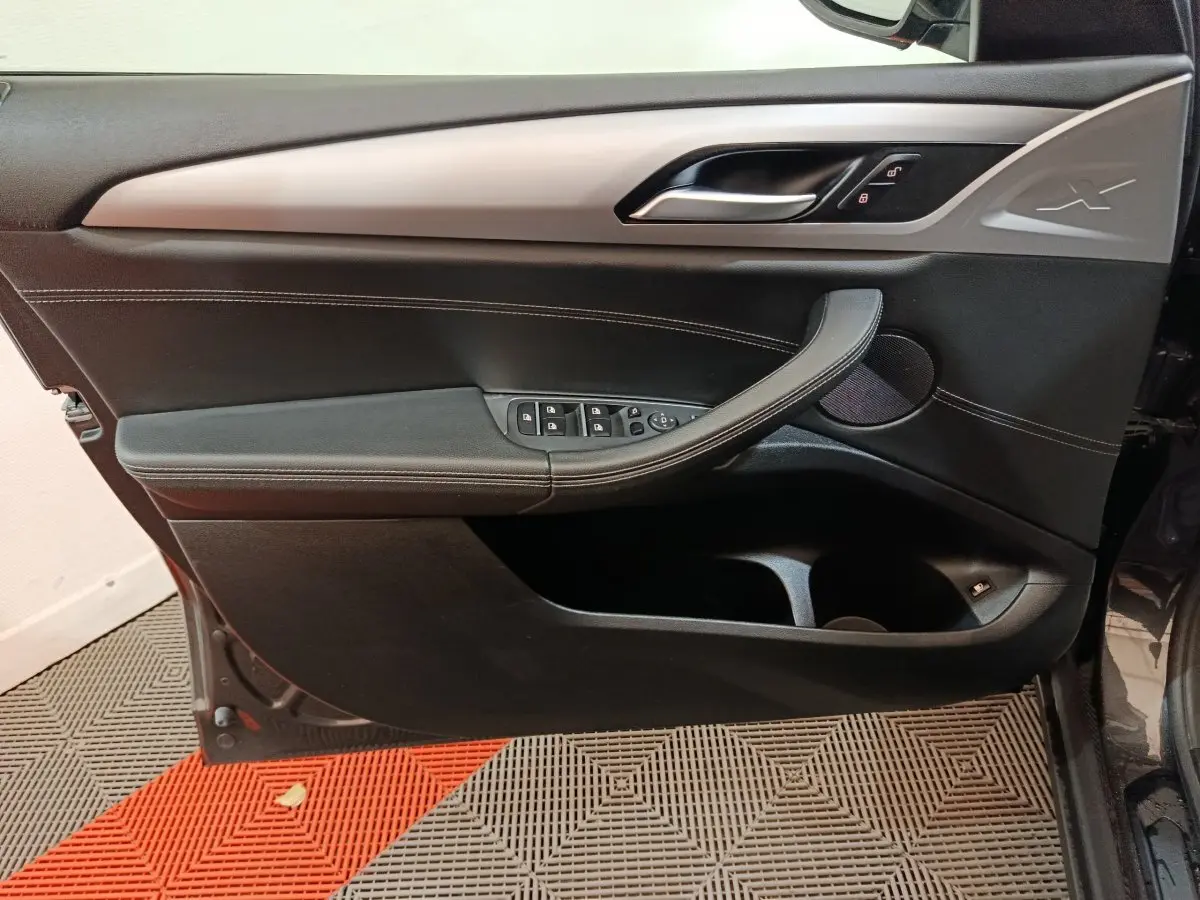 Vue intérieure côté gauche de la porte avant BMW X3 xDrive30e gris foncé avec commandes de vitres et logo X embossé.