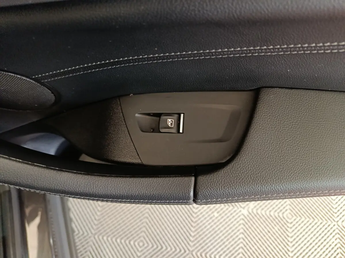 Détail du bouton de commande de vitre sur la porte intérieure noire d’un BMW X3 xDrive30e gris foncé.