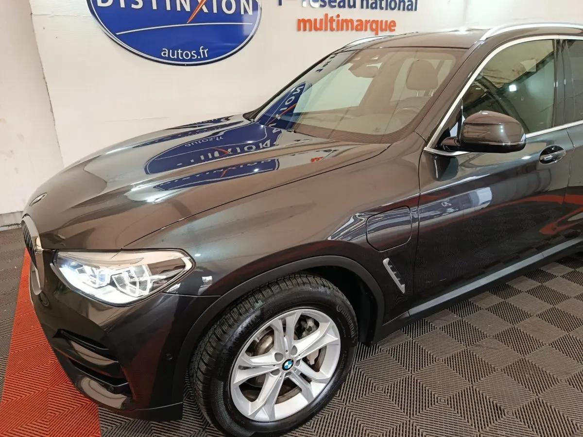 Vue 3/4 avant gauche d’un BMW X3 xDrive30e gris foncé avec jantes alliage et feux LED allumés.