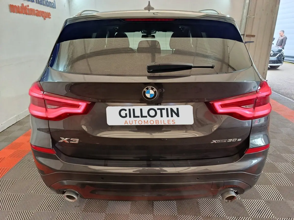 Vue arrière d’un BMW X3 xDrive30e gris foncé avec feux LED allumés et double sortie d’échappement visible.