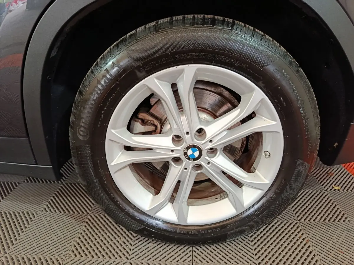 Gros plan sur la roue avant gauche avec jante argentée et logo BMW sur un BMW X3 gris foncé hybride rechargeable.