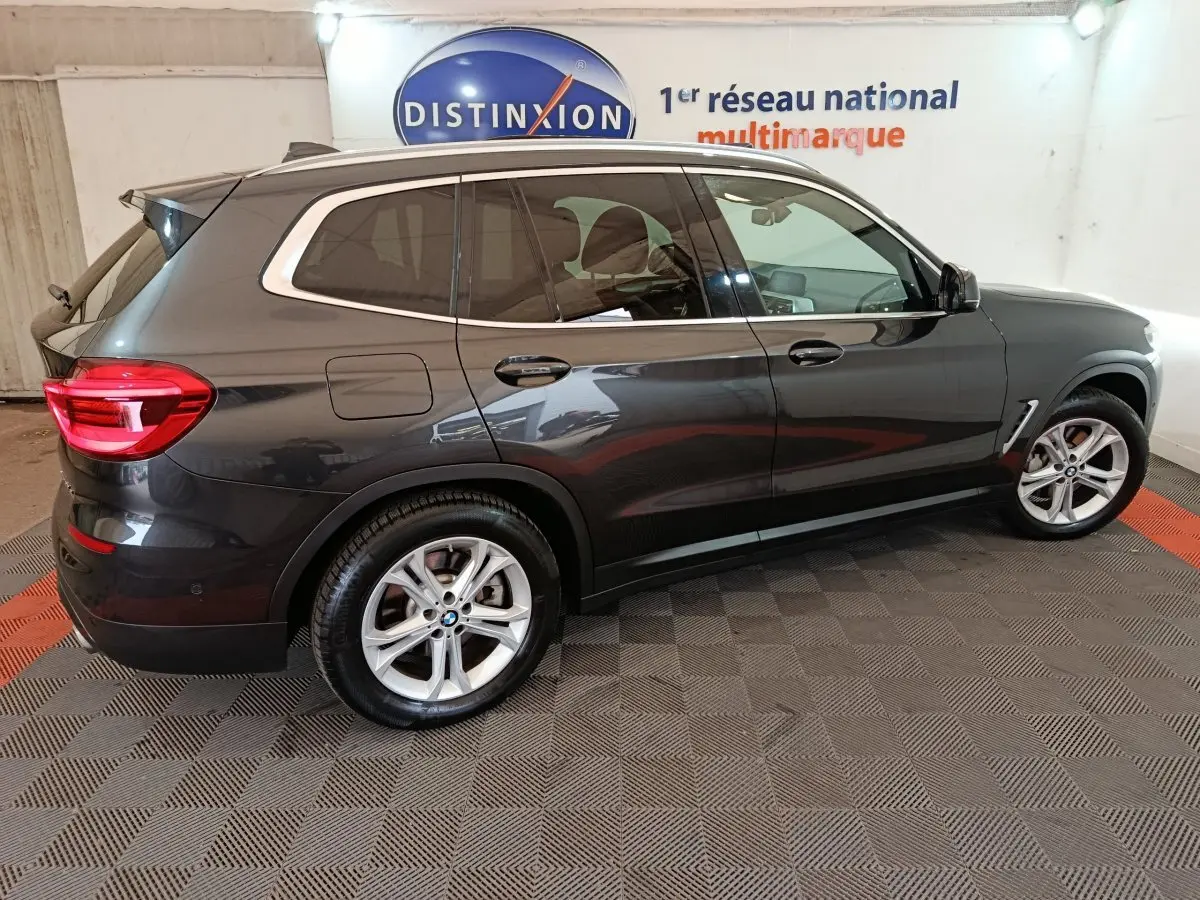 BMW X3 xDrive30e gris foncé vue de profil côté droit, avec jantes alliage et feux arrière allumés dans un showroom.
