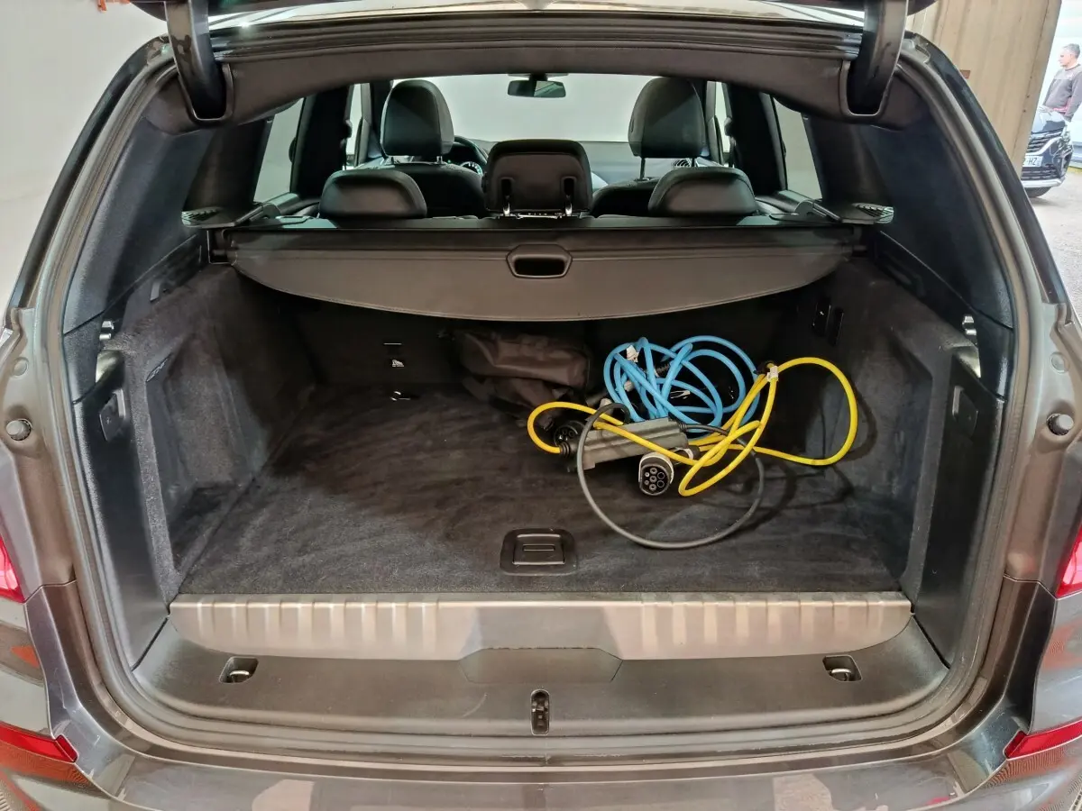 Vue arrière du coffre ouvert d'un BMW X3 gris foncé avec câbles de recharge hybrides visibles à l'intérieur.