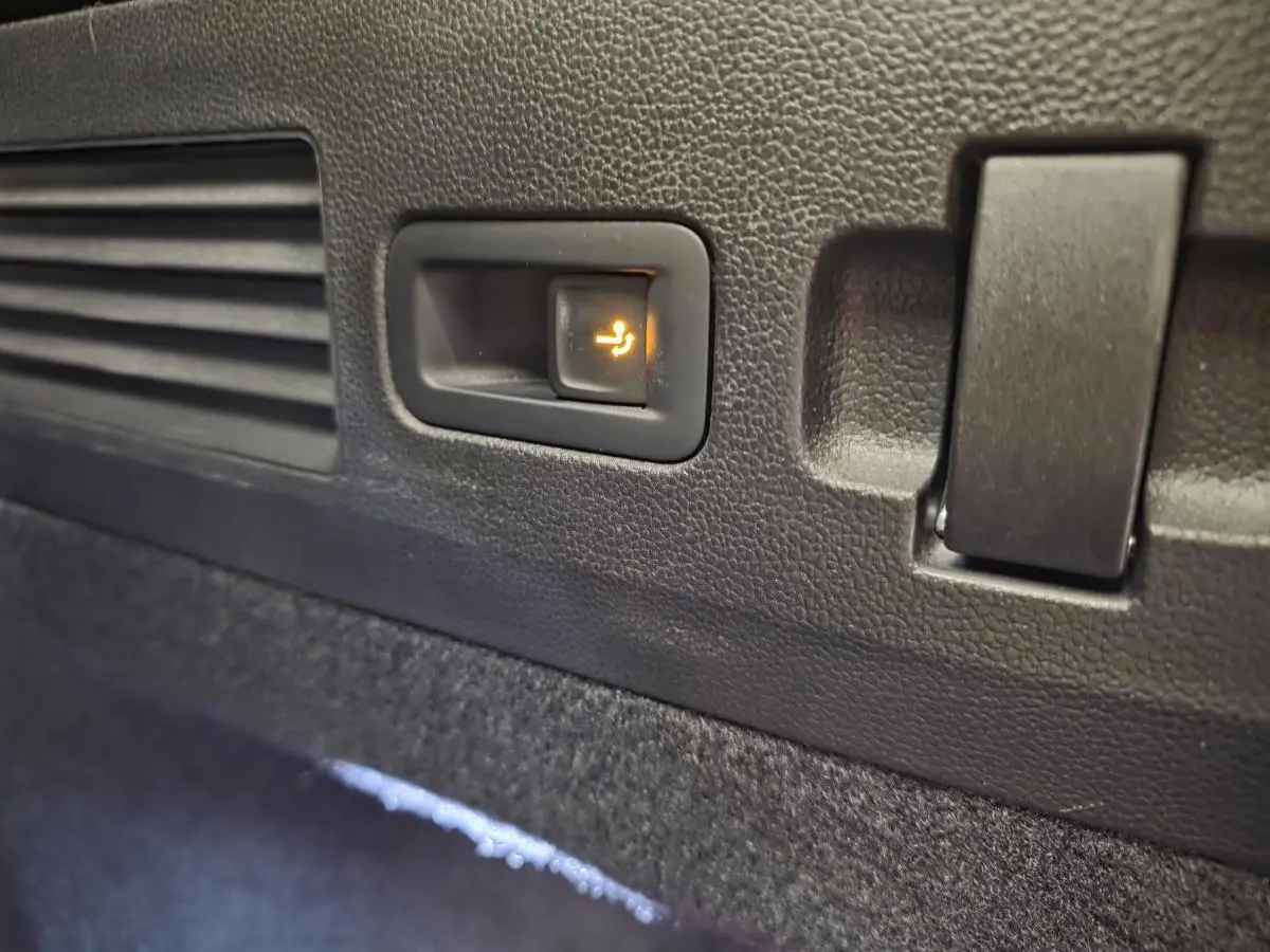 Gros plan sur le bouton d'abattement électrique des sièges arrière dans le coffre du Volkswagen Arteon gris Shooting Brake.