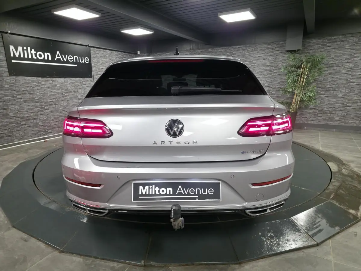 Vue arrière d'un Volkswagen Arteon gris avec feux LED allumés et dispositif d'attelage rabattable visible en intérieur showroom.