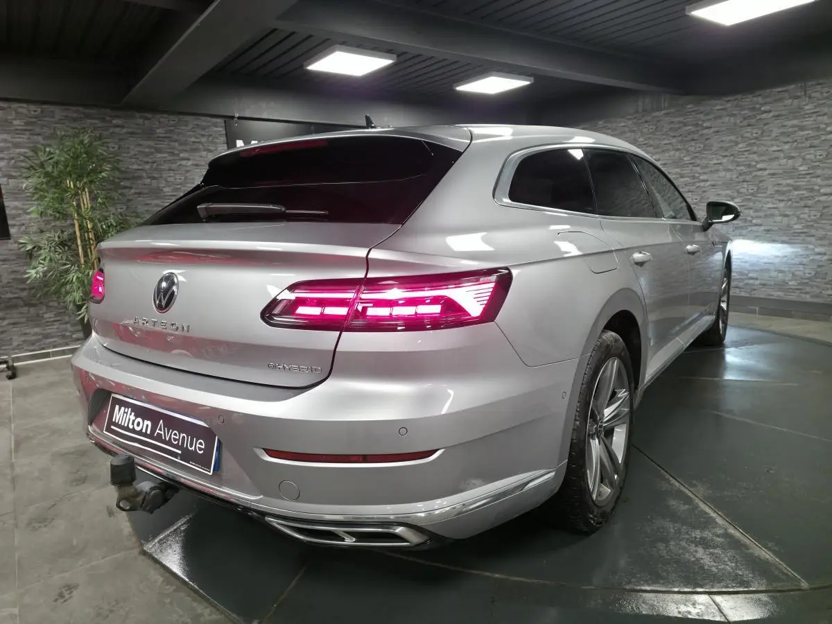 Vue 3/4 arrière droite d'une Volkswagen Arteon Shooting Brake gris métallisé avec feux arrière LED allumés et attelage rabattable.