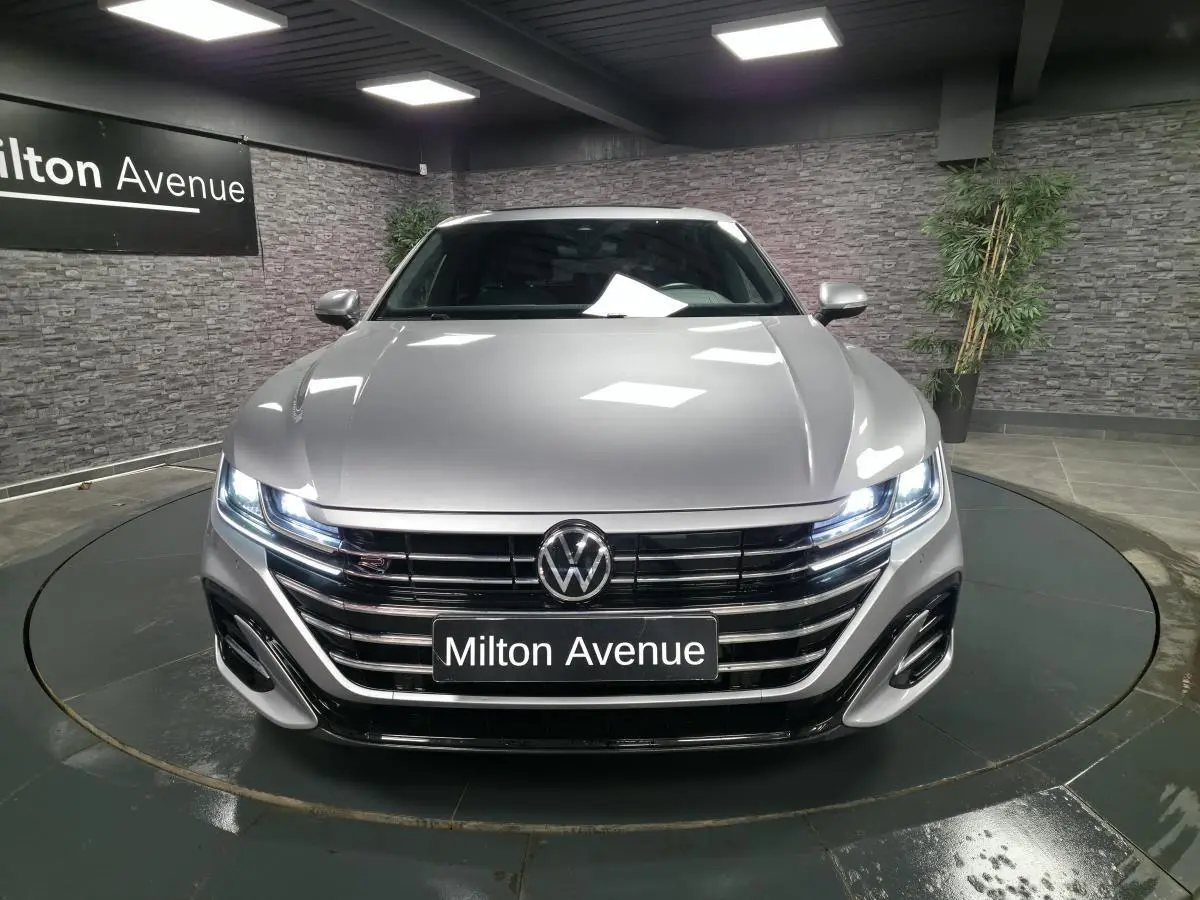 Vue avant d'une Volkswagen Arteon Shooting Brake gris métallisé avec calandre R-Line et phares LED allumés en showroom.