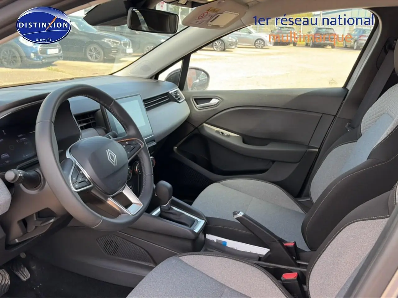 Vue intérieure côté conducteur de la Renault Clio V 2025, sièges gris clair avec motifs 3D et tableau de bord moderne.