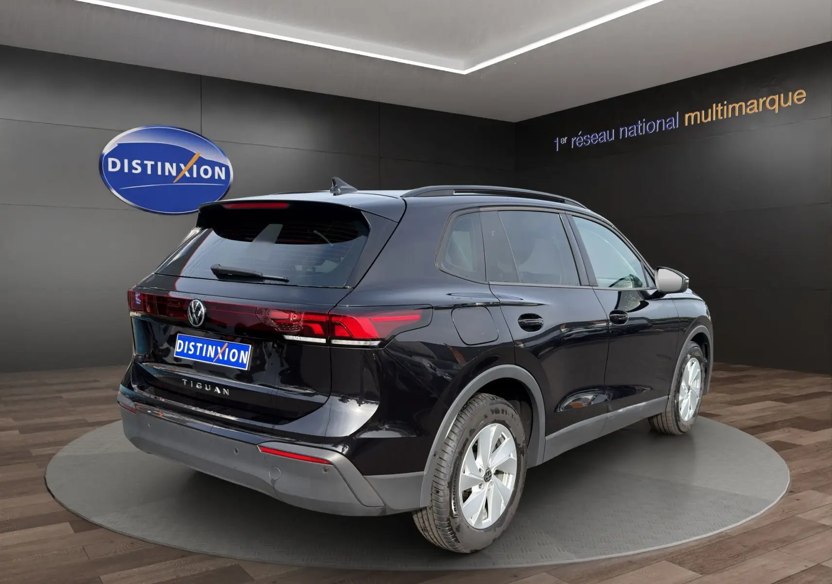Vue 3/4 arrière droite du Volkswagen Tiguan noir 2024 avec feux arrière LED et jantes argentées en showroom.