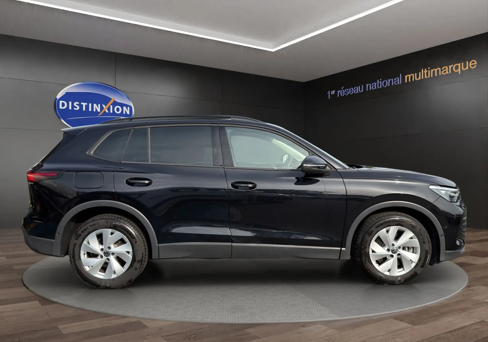 Vue de profil côté gauche d'un Volkswagen Tiguan noir 2024 dans un showroom avec jantes argentées.