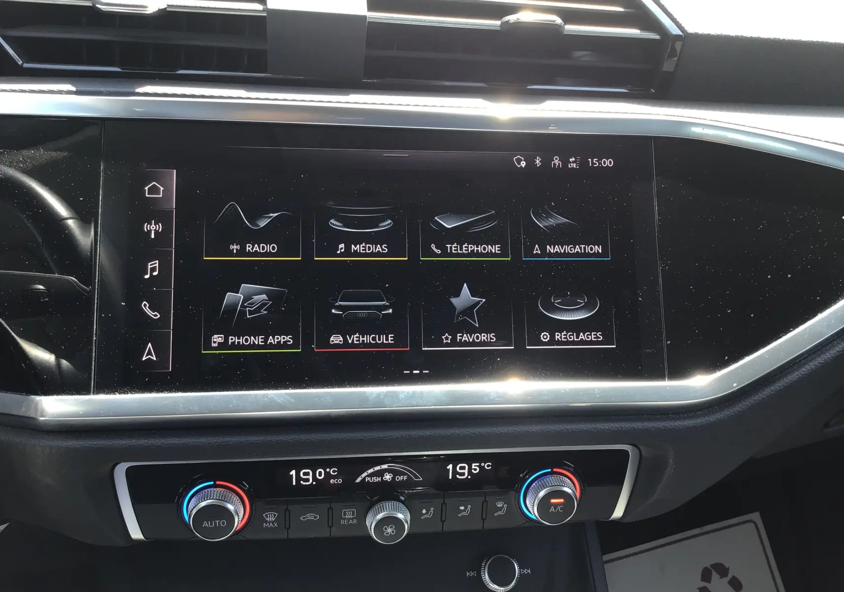 Vue rapprochée de l’écran tactile central et de la console de climatisation du tableau de bord d’un Audi Q3 Sportback gris clair métal.