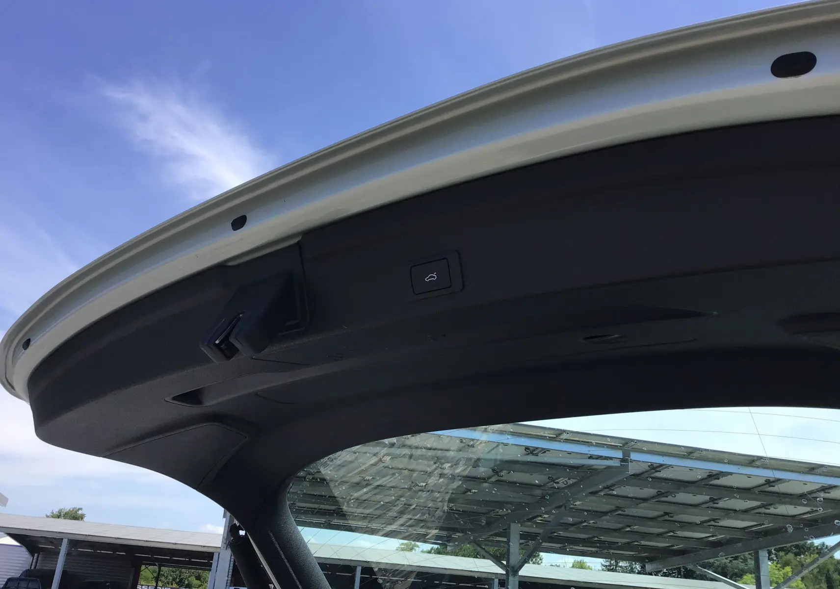 Vue en contre-plongée de la porte de coffre ouverte d’un Audi Q3 Sportback gris clair métal sous un ciel bleu.
