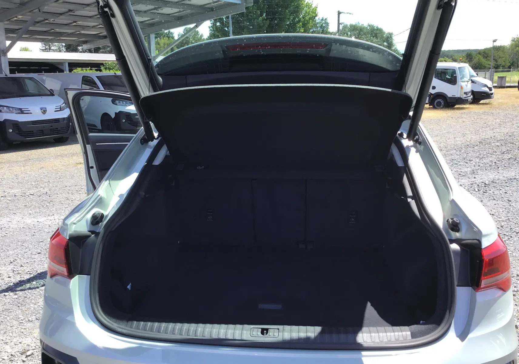 Coffre ouvert vu de l'arrière d'un Audi Q3 Sportback gris clair métal 2024, avec hayon relevé et intérieur spacieux.