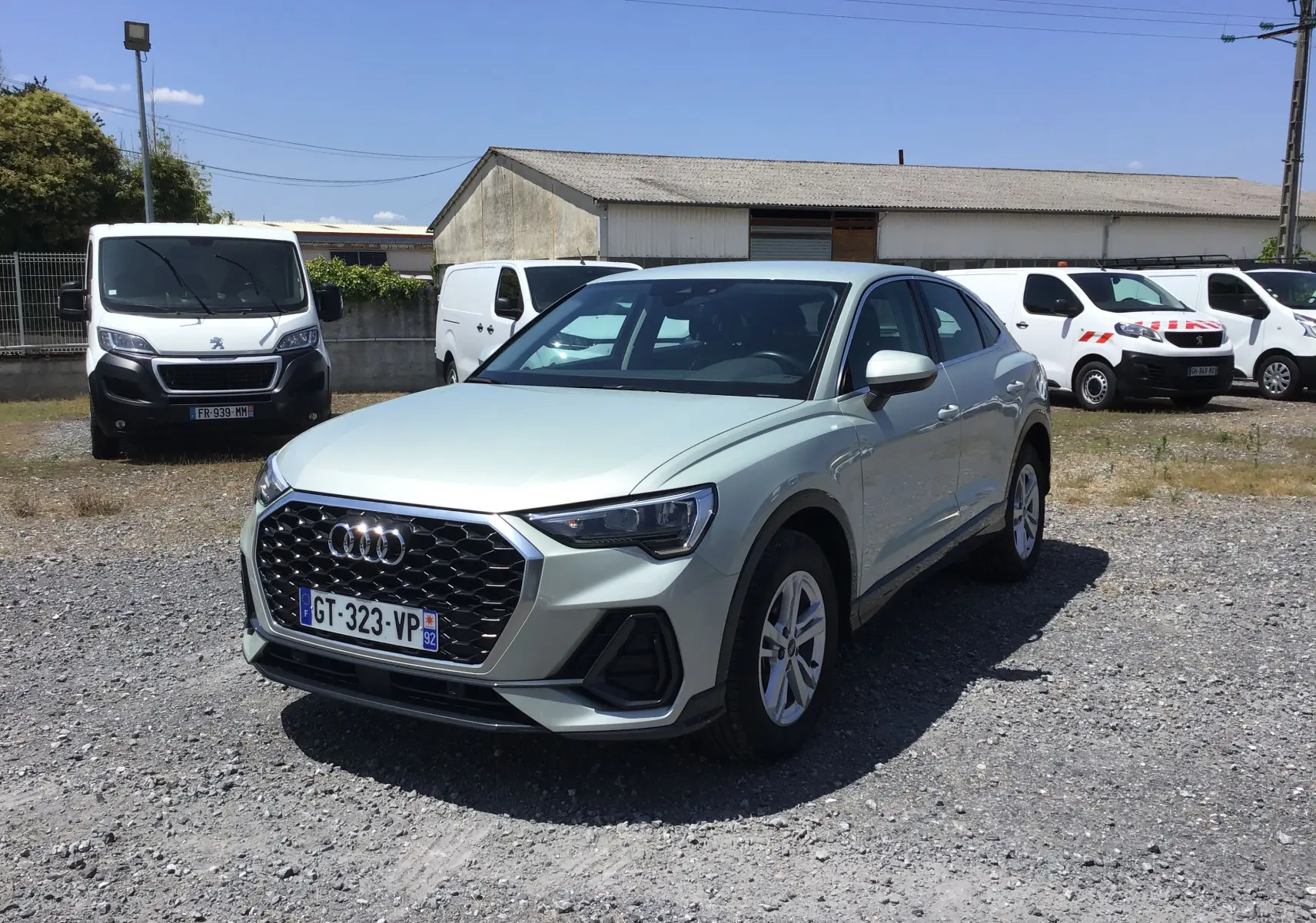 Audi Q3 Sportback gris clair métal vue 3/4 avant droit sur parking avec calandre noire à motifs hexagonaux.