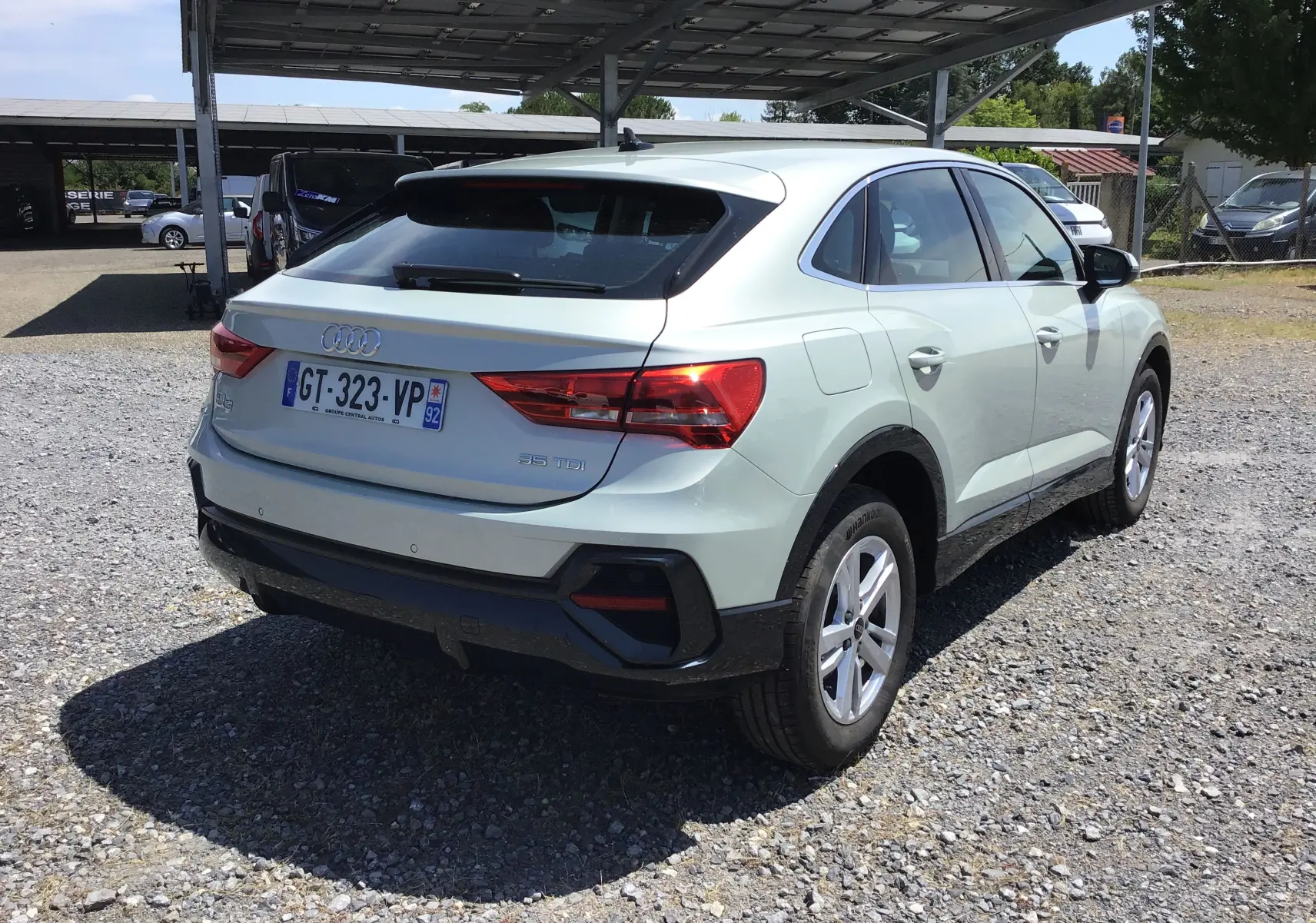 Audi Q3 Sportback gris clair métal vue 3/4 arrière droit, avec feux arrière allumés et jantes 17 pouces.