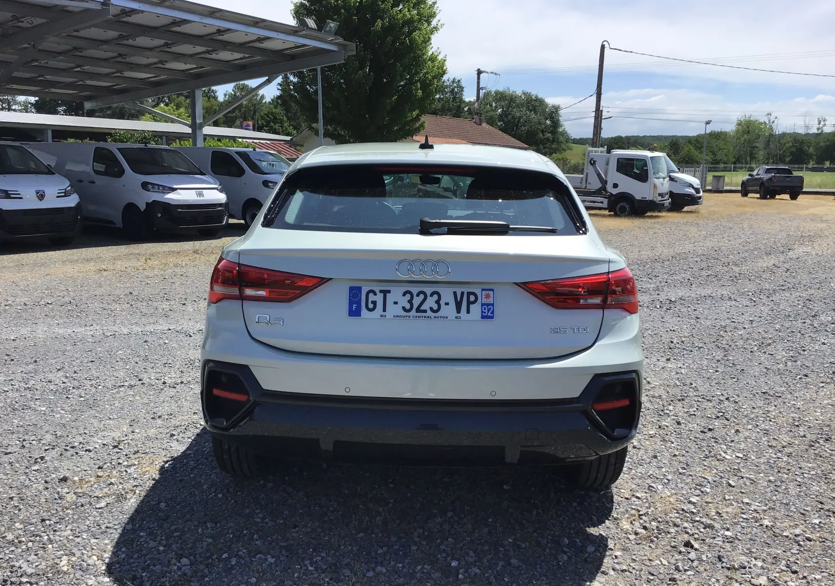 Vue arrière de l'Audi Q3 Sportback gris clair métal 2024, avec feux LED et badge 35 TDI visible sur un sol gravillonné.