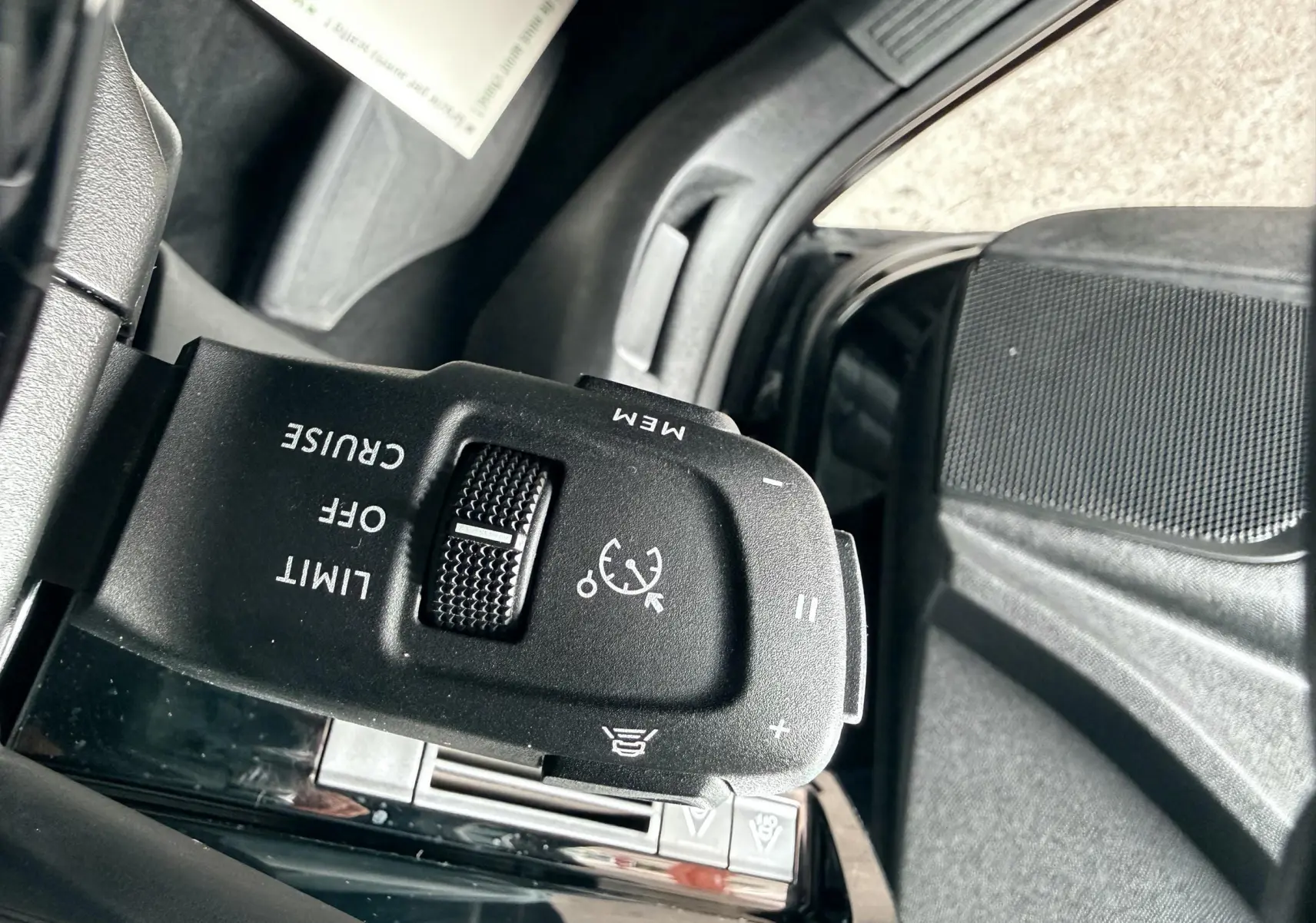 Gros plan sur la commande de régulateur de vitesse noir dans l'habitacle d'une Peugeot 308 SW noire.