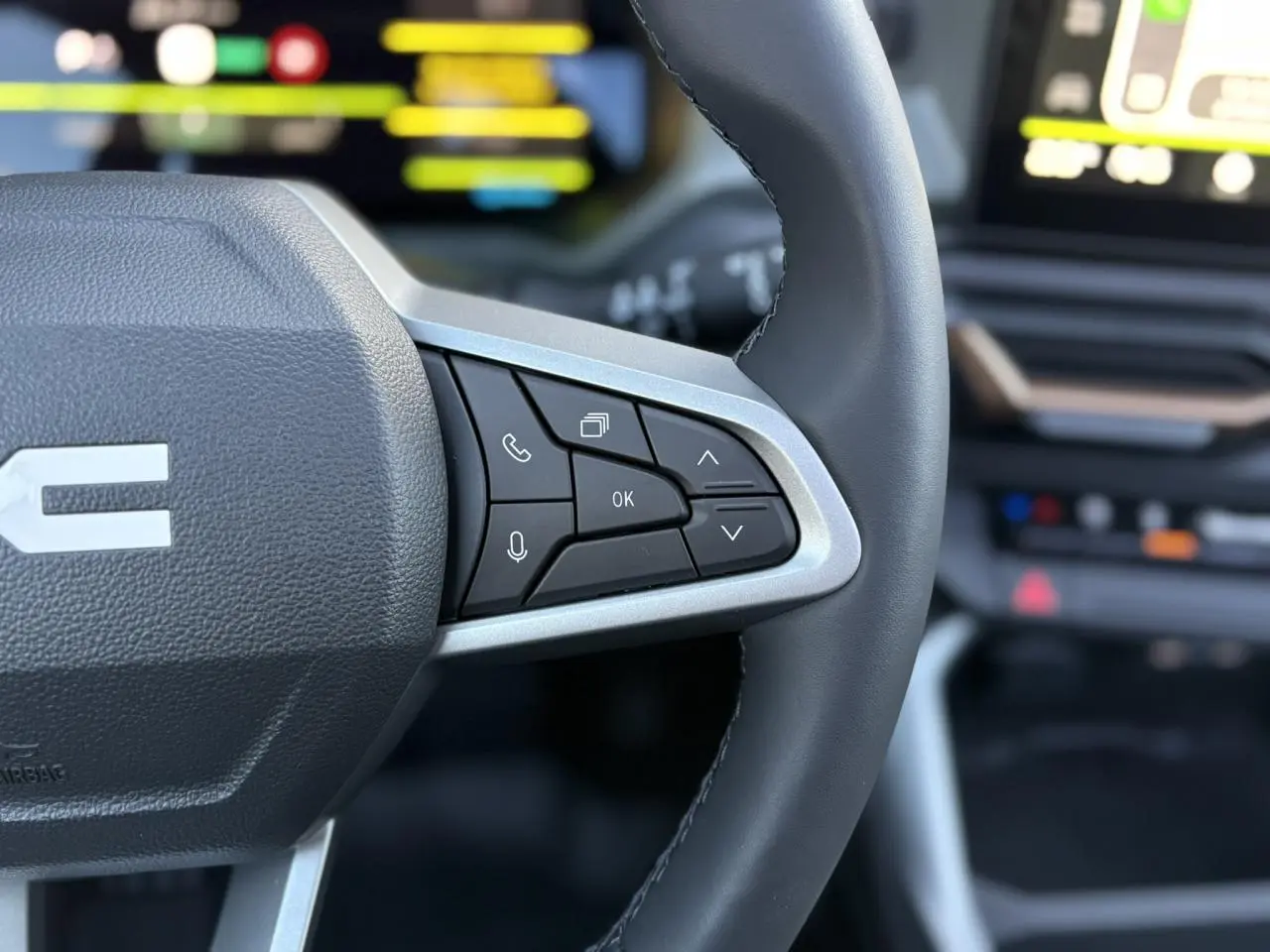 Gros plan sur le volant noir de la Dacia Bigster 2026 avec commandes multifonctions et tableau de bord numérique flou en arrière-plan.