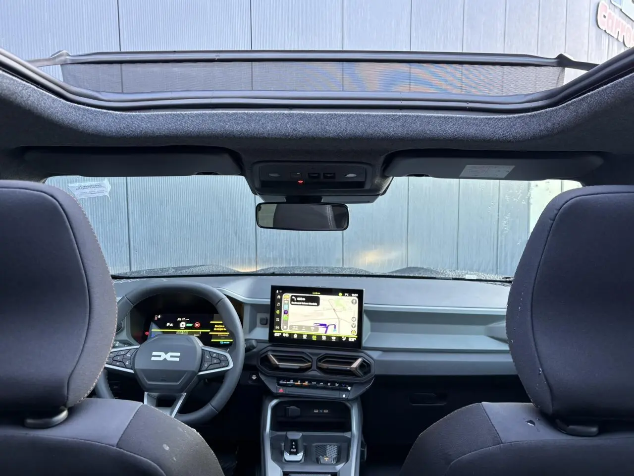 Vue intérieure avant du Dacia Bigster noir nacré, mettant en valeur le tableau de bord moderne et le toit panoramique.