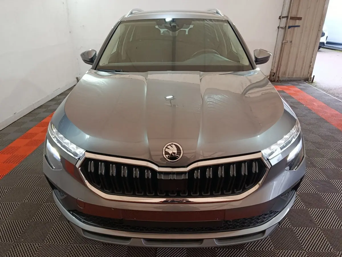 Vue frontale d'un Skoda Kamiq gris clair avec calandre chromée et phares LED allumés dans un garage.