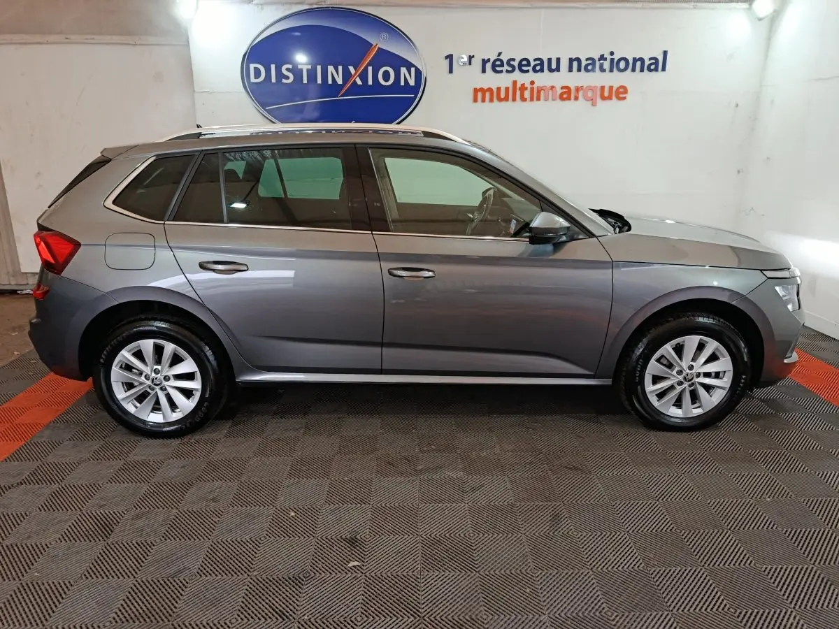 Vue de profil côté gauche d'un Skoda Kamiq gris clair 2024 dans un showroom avec toit ouvrant et jantes alliage.