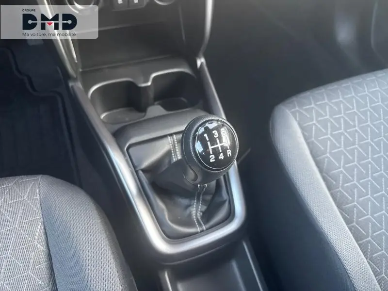 Le levier de vitesses manuel noir de la Suzuki Swift 1.2 Hybrid 83ch Pack, entouré des sièges tissu gris à motifs.