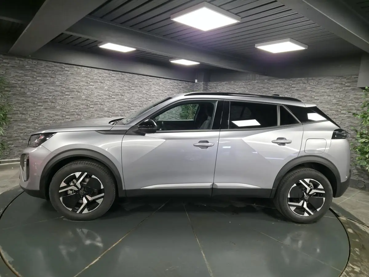 Vue latérale droite d'un Peugeot 2008 gris métallisé avec jantes bi-ton et toit noir en intérieur showroom.