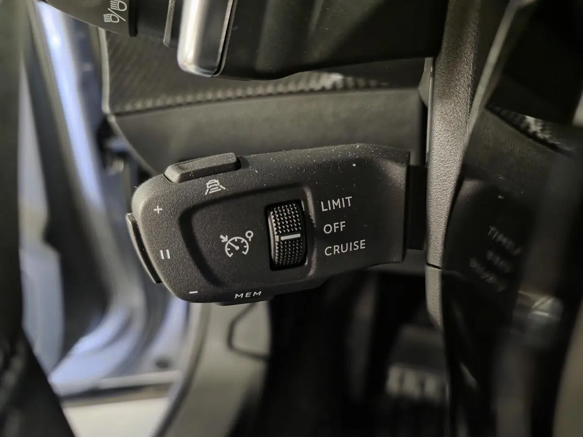 Gros plan sur la commande de régulateur de vitesse noir à gauche du volant dans le Peugeot 2008 gris 2025.
