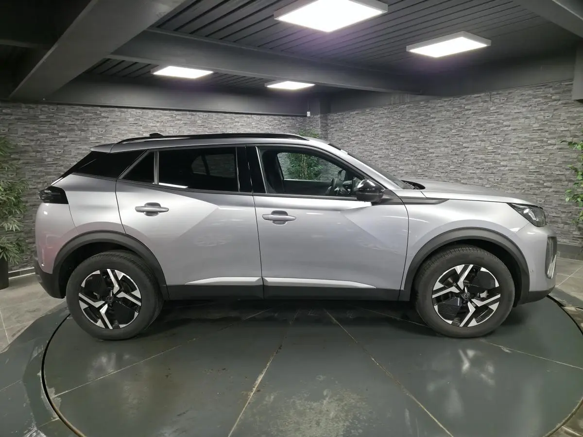 Peugeot 2008 gris en profil droit dans un showroom, avec jantes alliage bi-ton et vitres teintées.