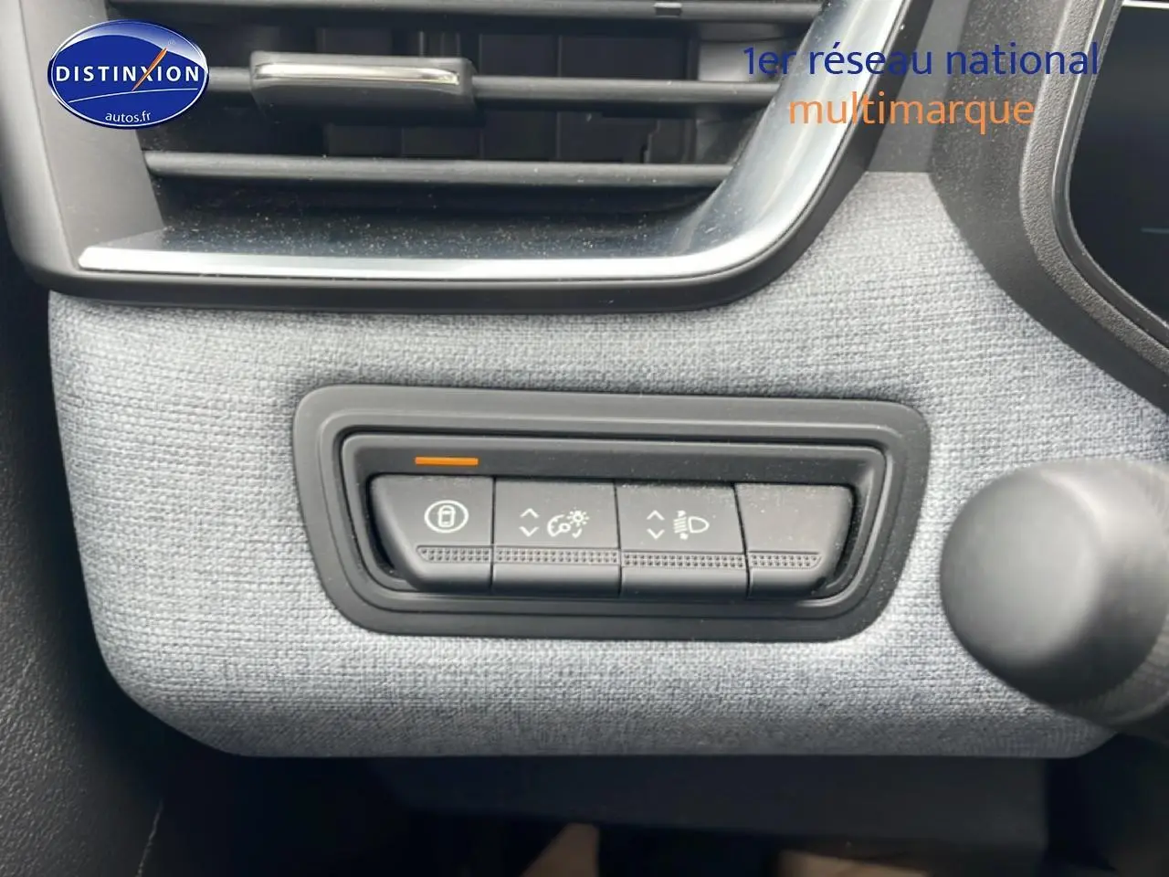Gros plan sur les commandes d’éclairage et verrouillage sur tableau de bord gris de la Renault Clio V blanche.