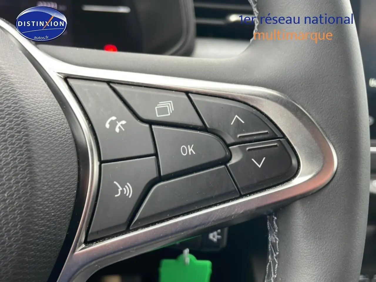 Gros plan sur les commandes multifonctions noires du volant de la Renault Clio V blanche, avec finition argentée.