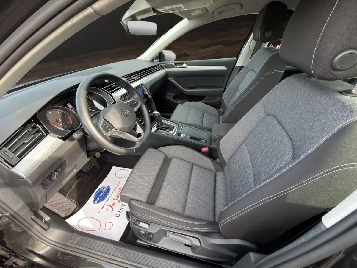 Vue intérieure côté conducteur de la Volkswagen Passat 2.0 TDI 2022 avec sièges tissu gris et tableau de bord moderne.