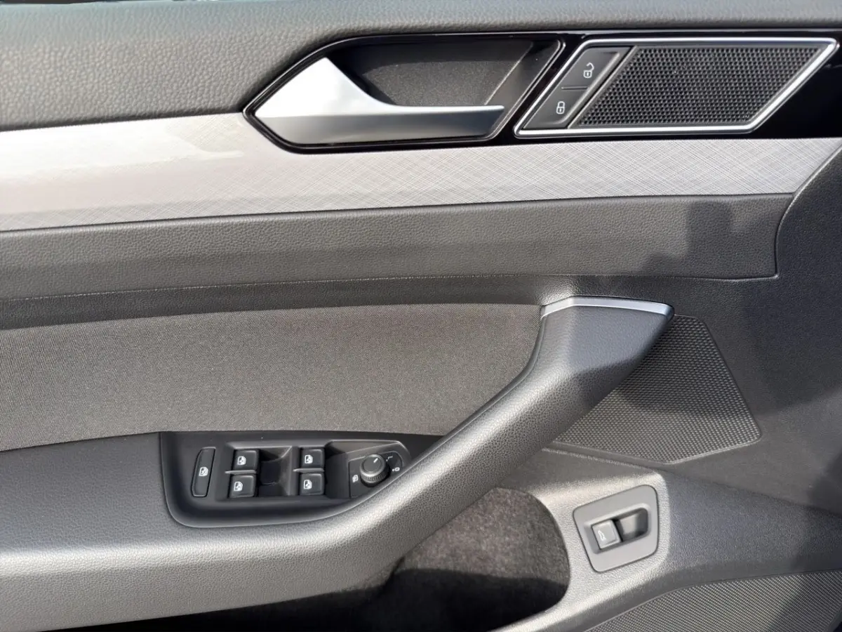 Gros plan sur la porte côté conducteur de la Volkswagen Passat gris foncé, avec commandes électriques et poignée intégrée.