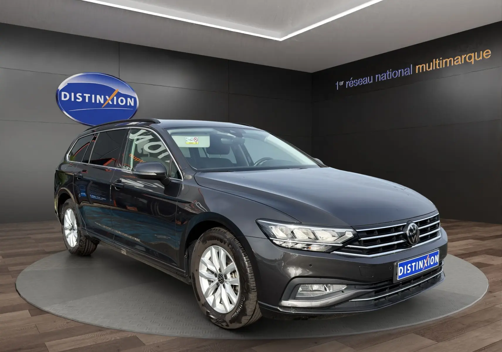 Volkswagen Passat break gris foncé vue 3/4 avant en intérieur avec jantes alliage et calandre chromée.