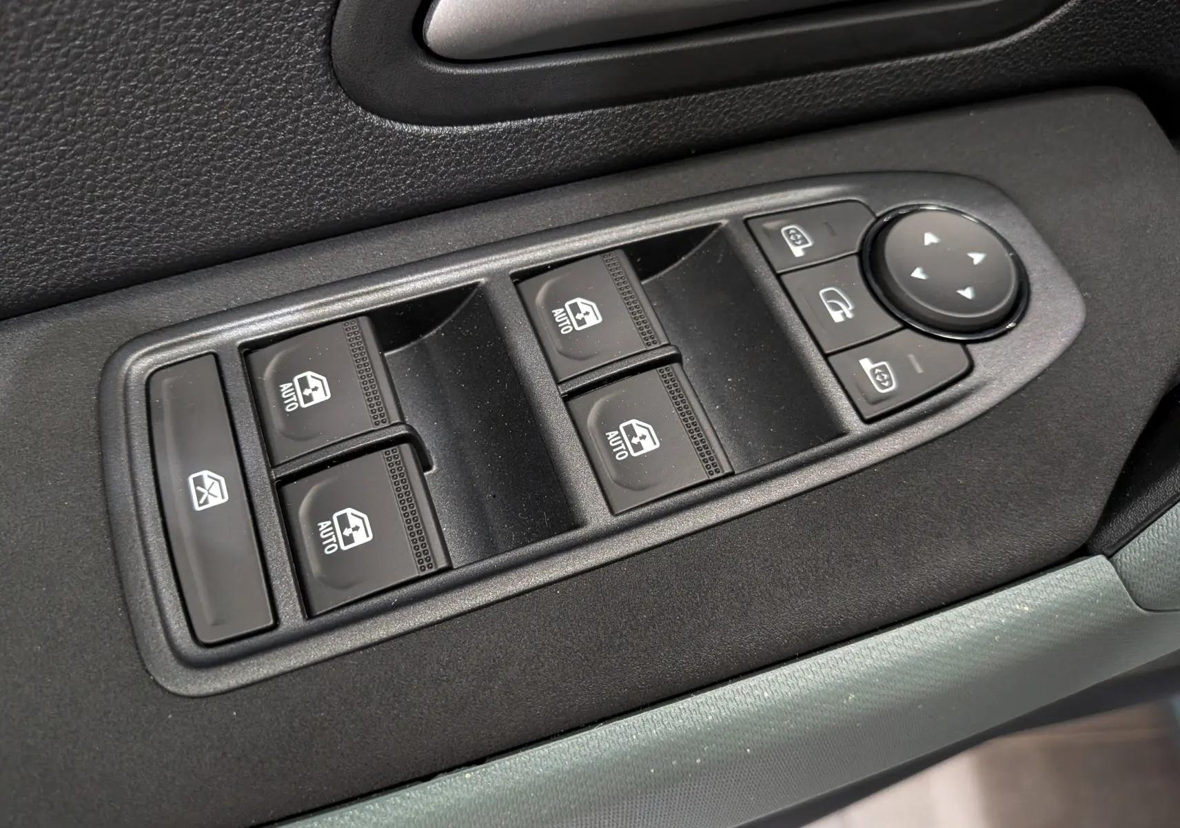 Gros plan sur les commandes de lève-vitres et rétroviseurs électriques côté conducteur du Dacia Duster gris Schiste 2026.