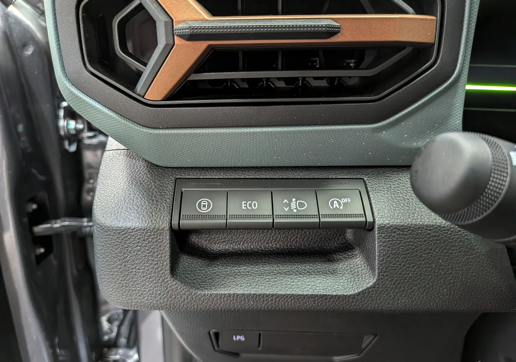 Gros plan sur les commandes noires et la grille d’aération avec insert marron du tableau de bord du Dacia Duster gris schiste.