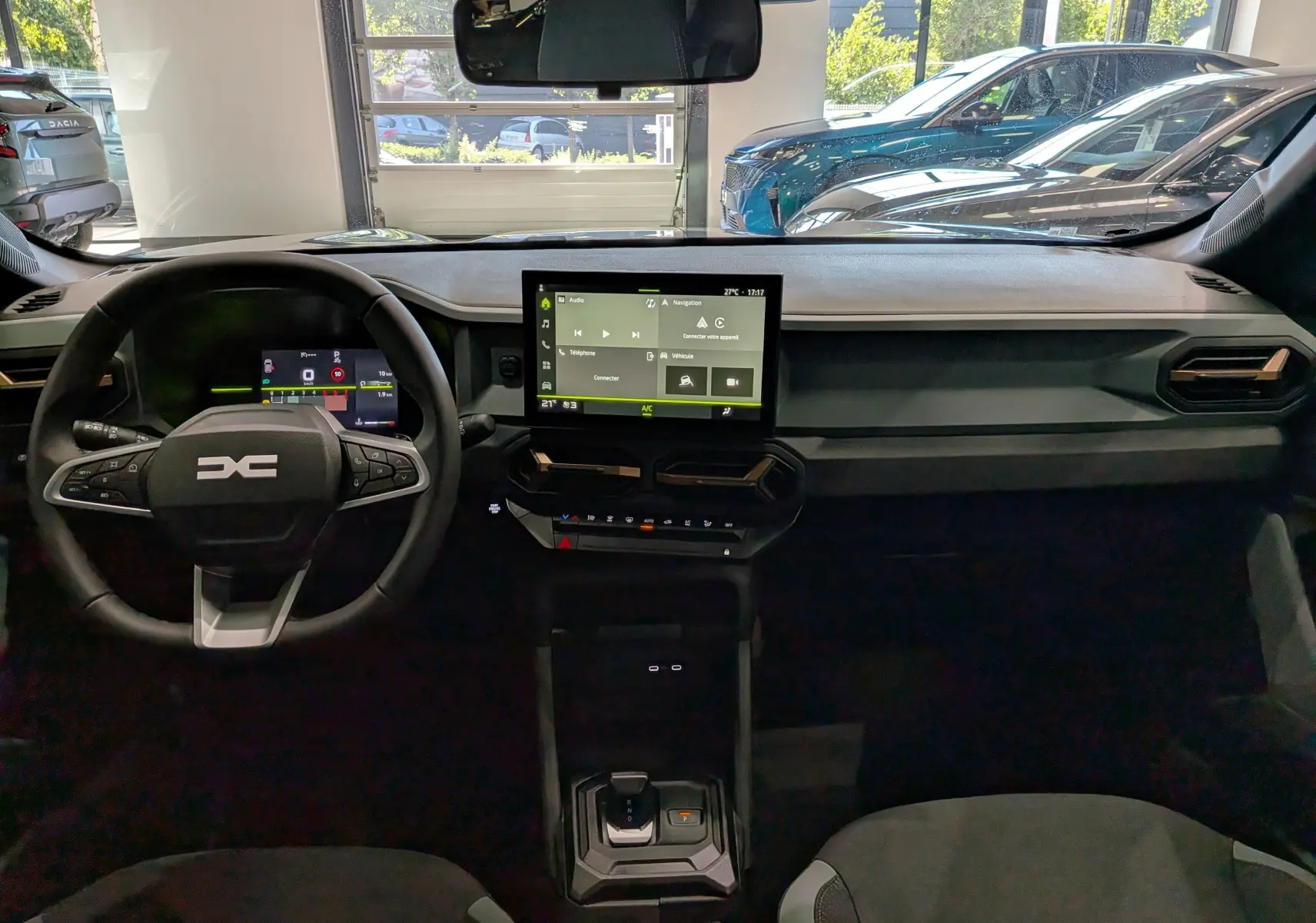 Vue intérieure frontale du tableau de bord du Dacia Duster 2026 avec écran tactile central et volant multifonction noir.