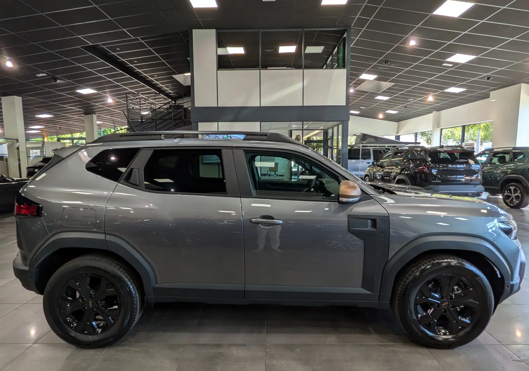 Vue de profil côté gauche du Dacia Duster 2026 gris schiste avec jantes noires et détails noirs mats en concession.