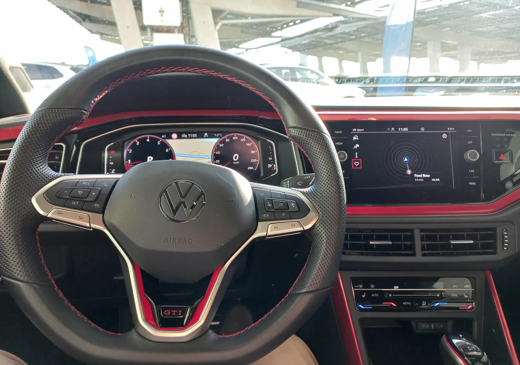 Vue intérieure centrée sur le volant noir avec surpiqûres rouges et tableau de bord numérique de la Volkswagen Polo GTI 2024.