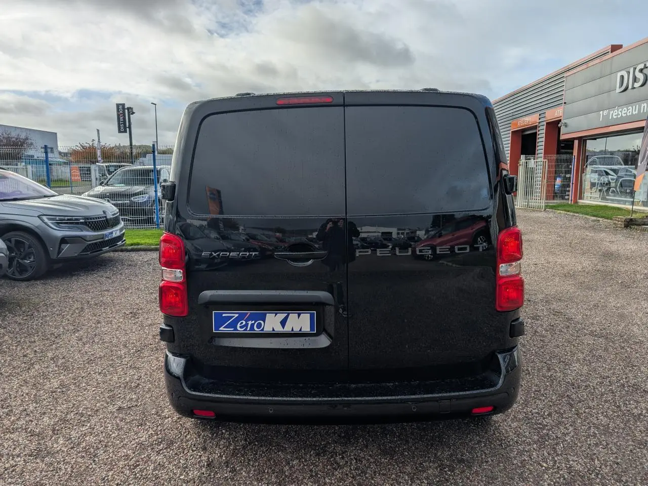 Vue arrière d'un Peugeot Expert Fourgon noir avec portes battantes et feux rouges visibles sur un parking.