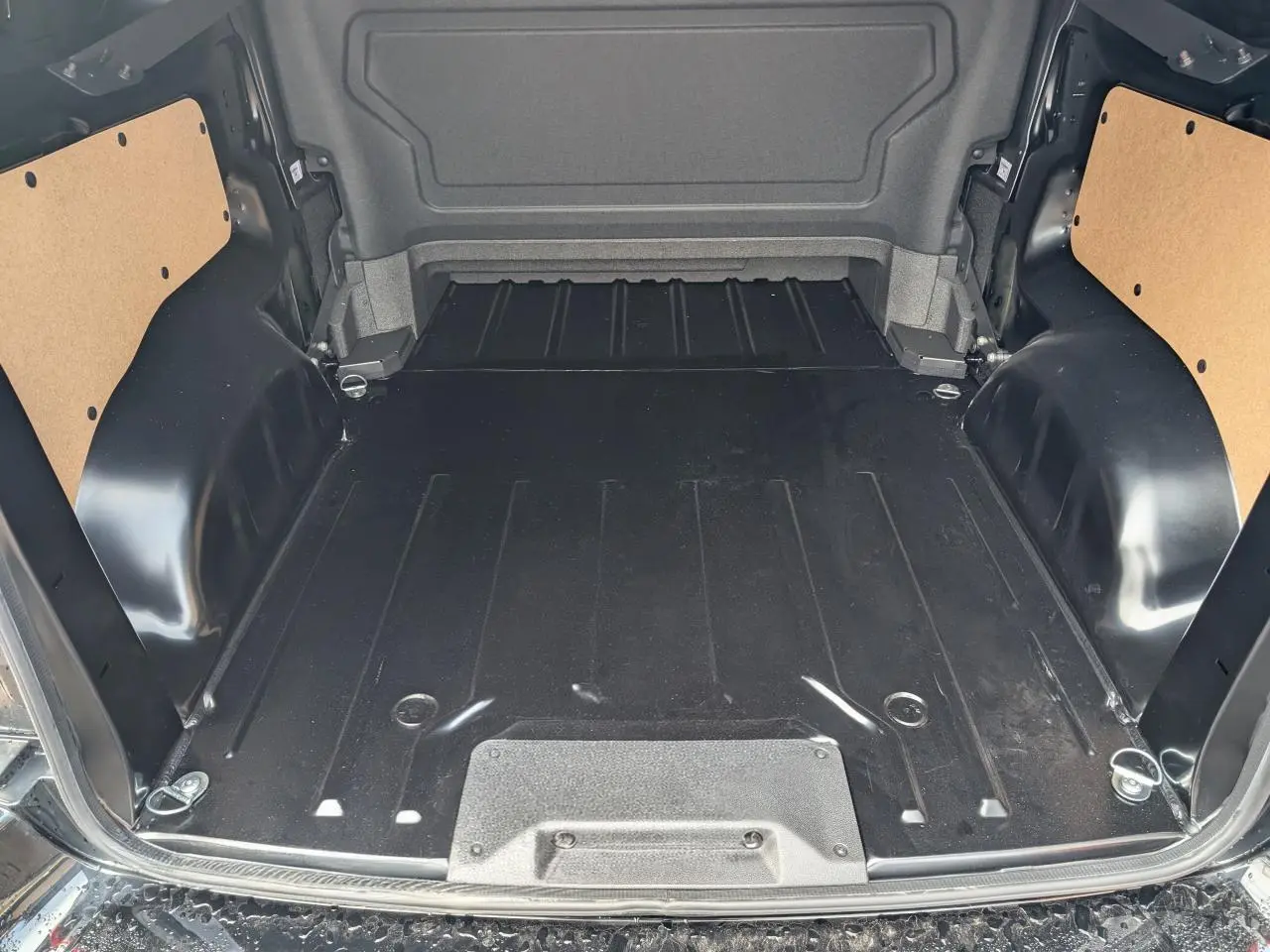 Espace de chargement noir du Peugeot Expert Fourgon 2025, vue arrière ouverte avec fixations et panneaux latéraux bois.
