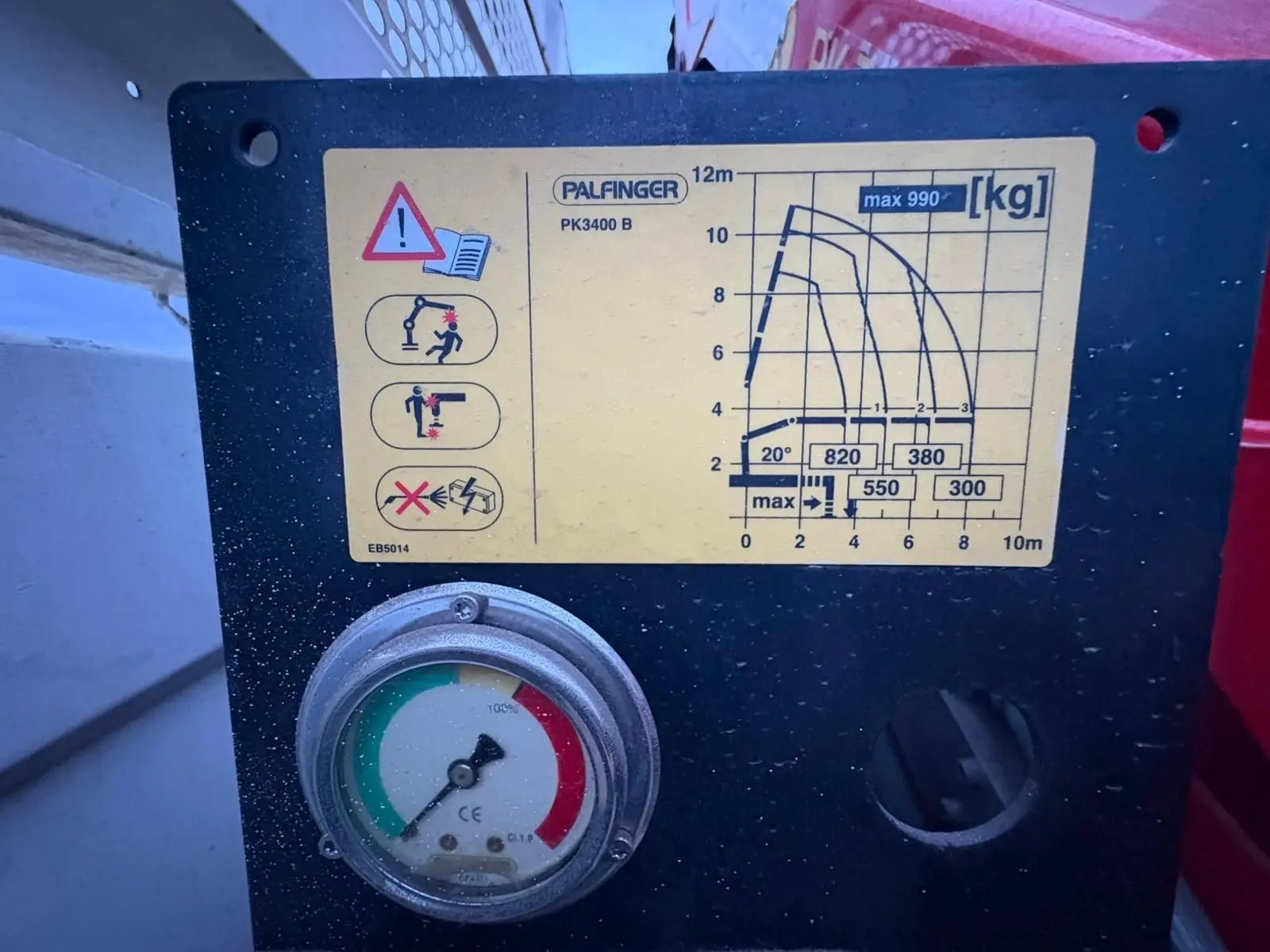 Gros plan sur le panneau de contrôle noir avec étiquette jaune et manomètre de la grue Palfinger sur véhicule blanc.