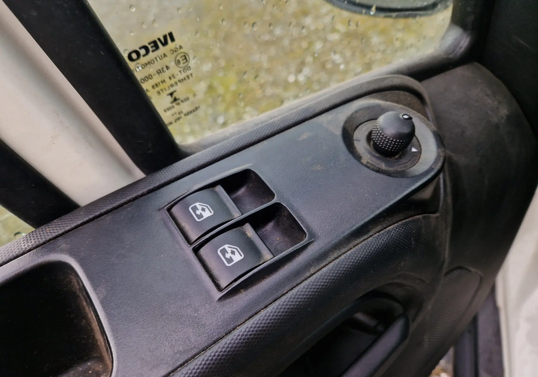 Gros plan sur les commandes de lève-vitres et réglage des rétroviseurs côté conducteur d’un Iveco Daily Chassis Cabine blanc.