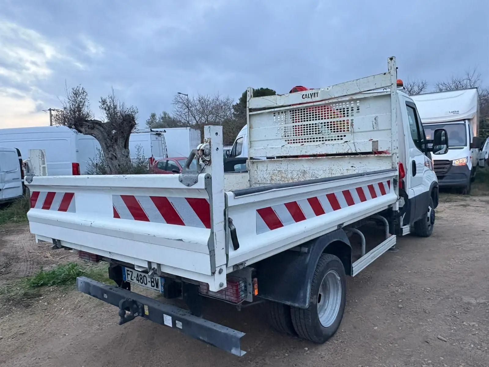 IVECO Daily Chassis Cabine blanc vu 3/4 arrière droit avec benne et grue Palfinger, marquages rouges et blancs.